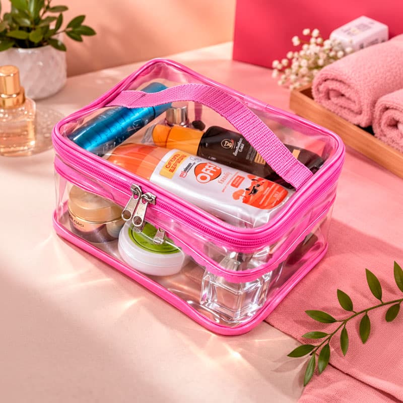 Uma necessaire de cristal transparente com detalhes rosas vista de cima com diversos itens de maquiagens e cosméticos dentro.