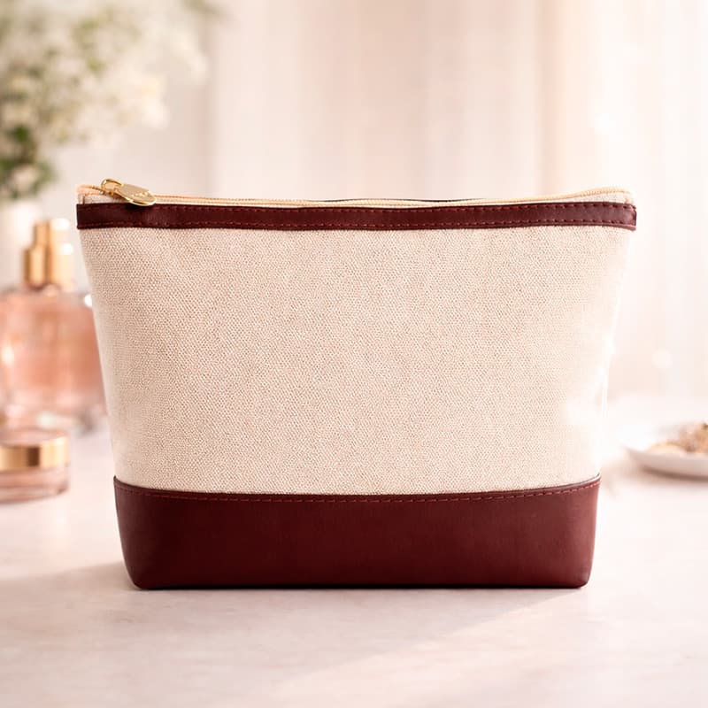 uma necessaire na cor bege e bordô sobre uma mesa em um ambienteiluminado com alguns itens ao fundo